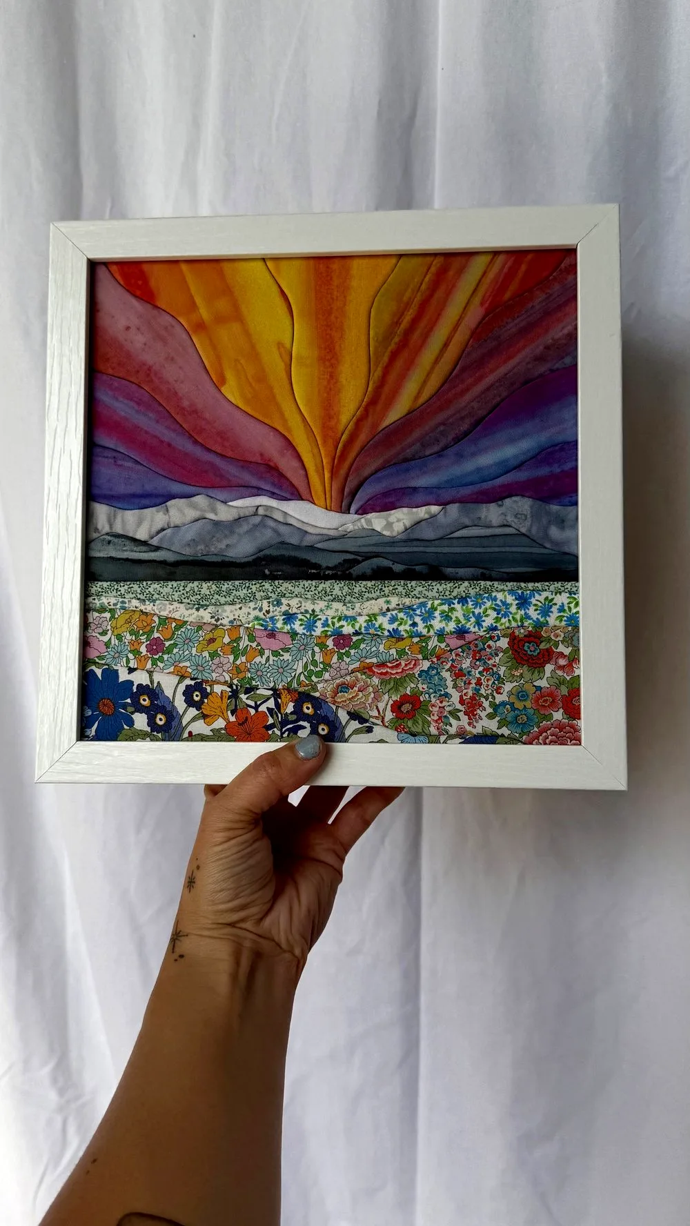 Hannah holding the finished 9 by 9 inch kinusaiga sunrise landscape in a white shadow box frame